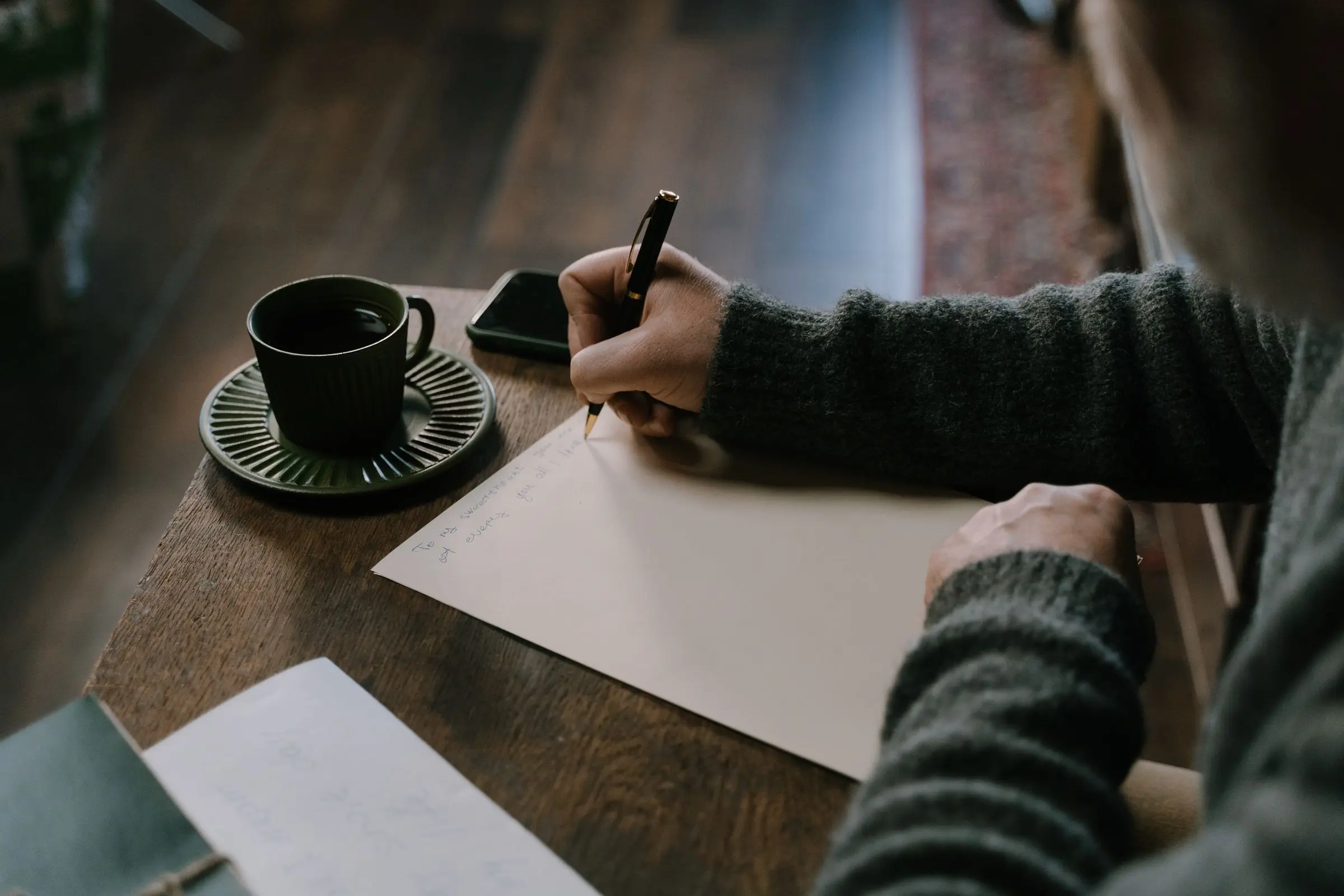 Hands writing notes on paper beside a cup of coffee