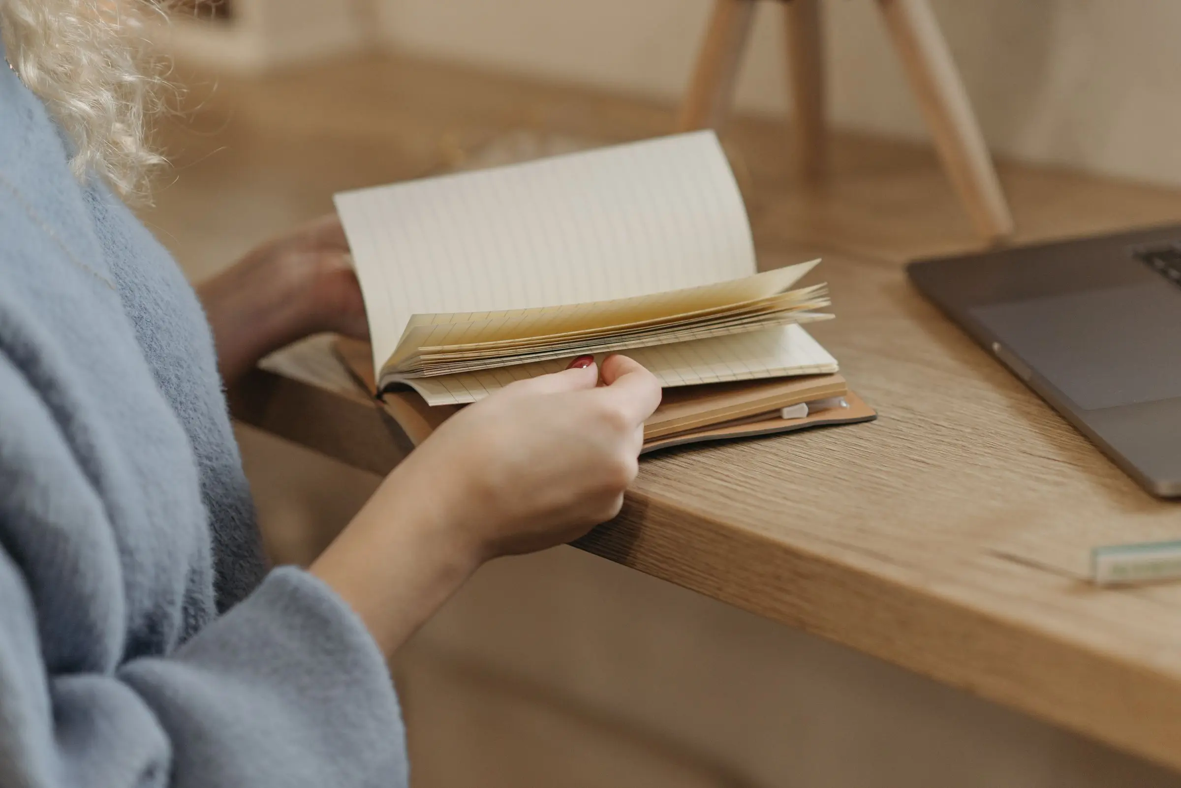 Hands turning the pages of a notebook at a wooden table