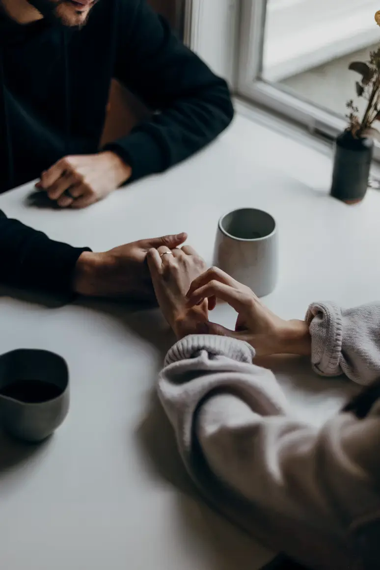 Two people sitting at a table with coffee, hands gently touching