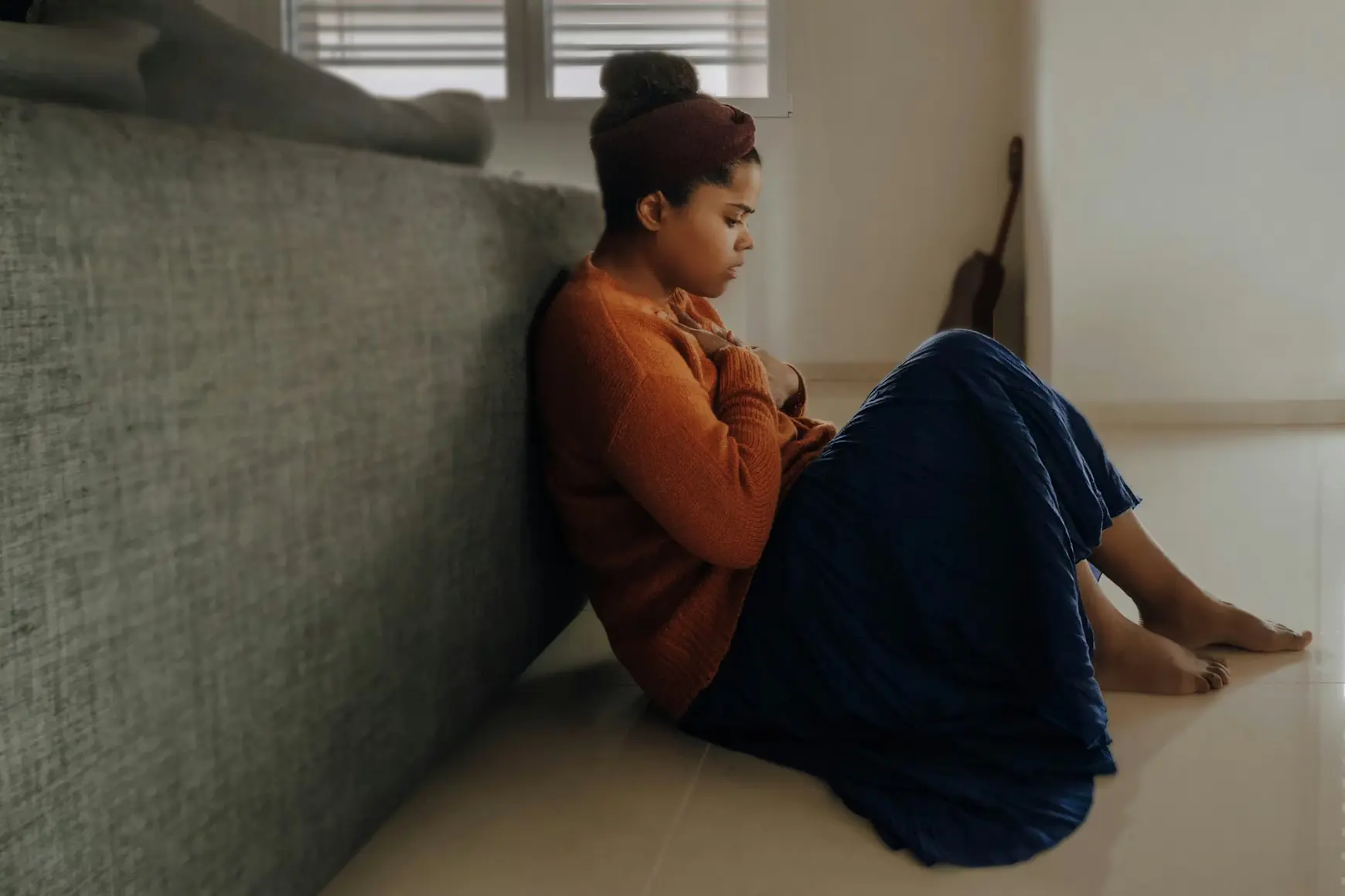 A young adult sits quietly against a couch, reflecting