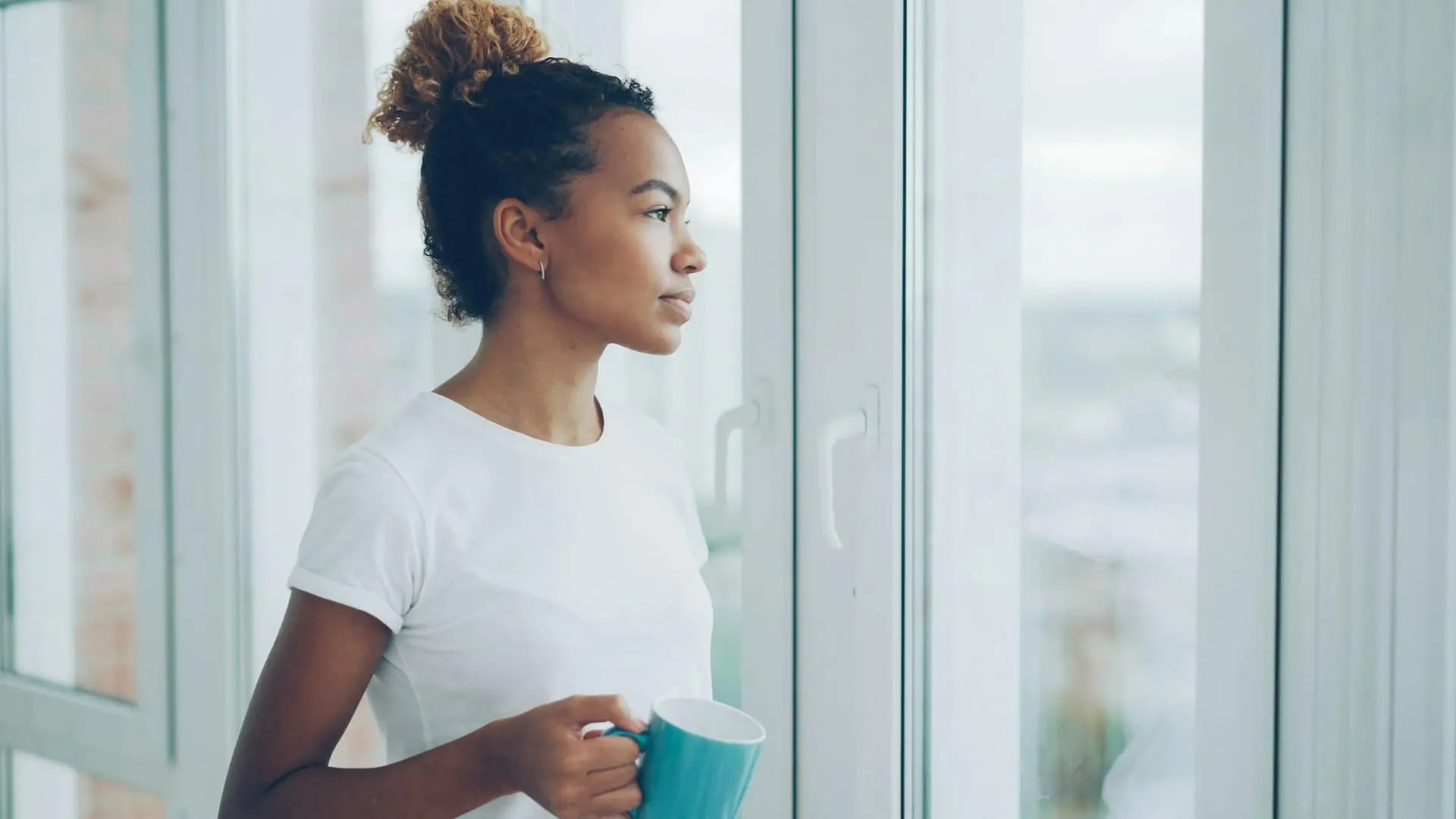 A woman holding a mug, looking out of a large window